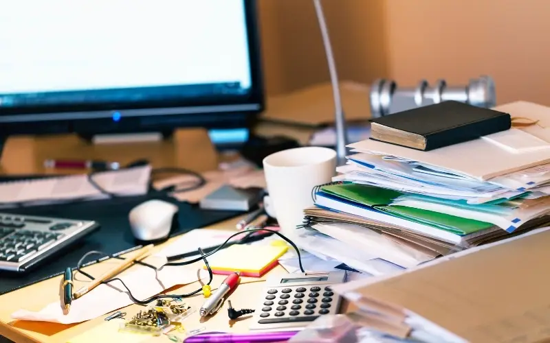 A disorganized desk with a computer on it and a stack of papers with Bible atop it. A disorganized desk with a computer on it and a stack of papers with Bible atop it.